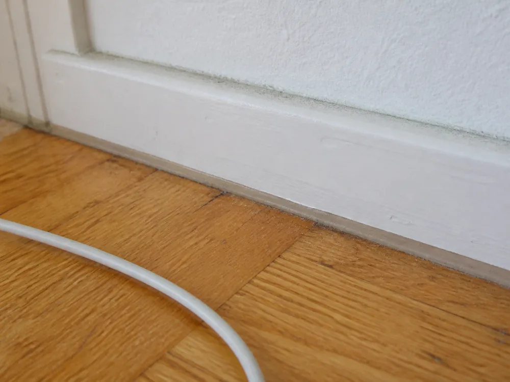 Detail des Übergangs zwischen Eichenparkett und weißer Sockelleiste