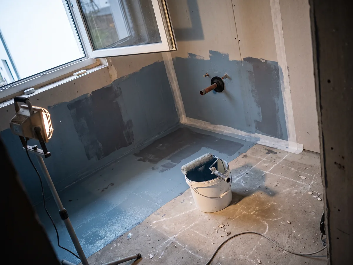 Bad vor dem Verfliesen: flüssig aufgetragene Verbundabdichtung auf Wand und Boden, Dichtband in der Ecke und Manschette am Rohrdurchgang