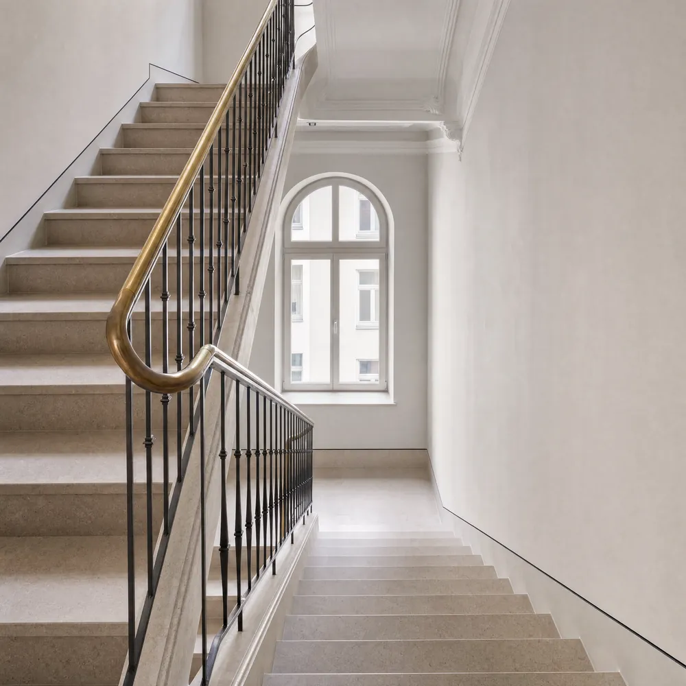 Treppenhaus im Altbau mit Kalksteinstufen, gefasster Trittkante und Messinghandlauf auf schlanker Stahlbrüstung