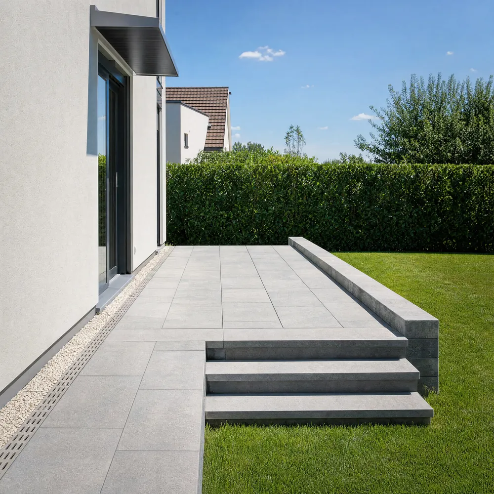 Terrasse mit Natursteinplatten im Splittbett, Blockstufen zum Rasen, Kiesstreifen und Entwässerungsrinne an der Hauswand